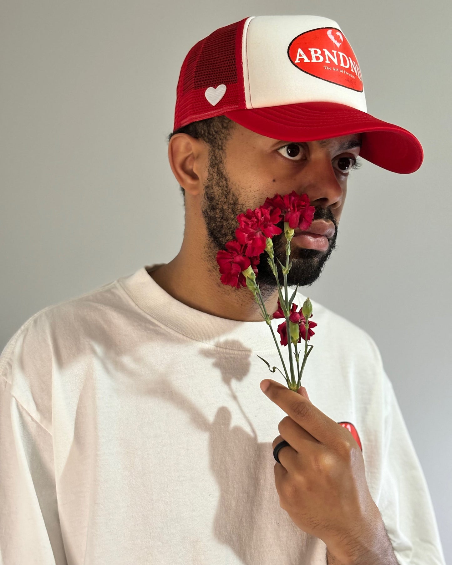 Heart & Freedom Trucker Hat worn by a model with red flowers, featuring distressed ABNDND patch and mesh back.